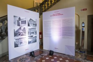 Due pannelli informativi all'interno di un edificio, uno con fotografie in bianco e nero di Villa Vittoria e l'altro con testi che raccontano la sua storia. Il pavimento è in marmo decorato e si vedono anche luci scaricate a terra. Sullo sfondo, una scala con ringhiera decorata.
