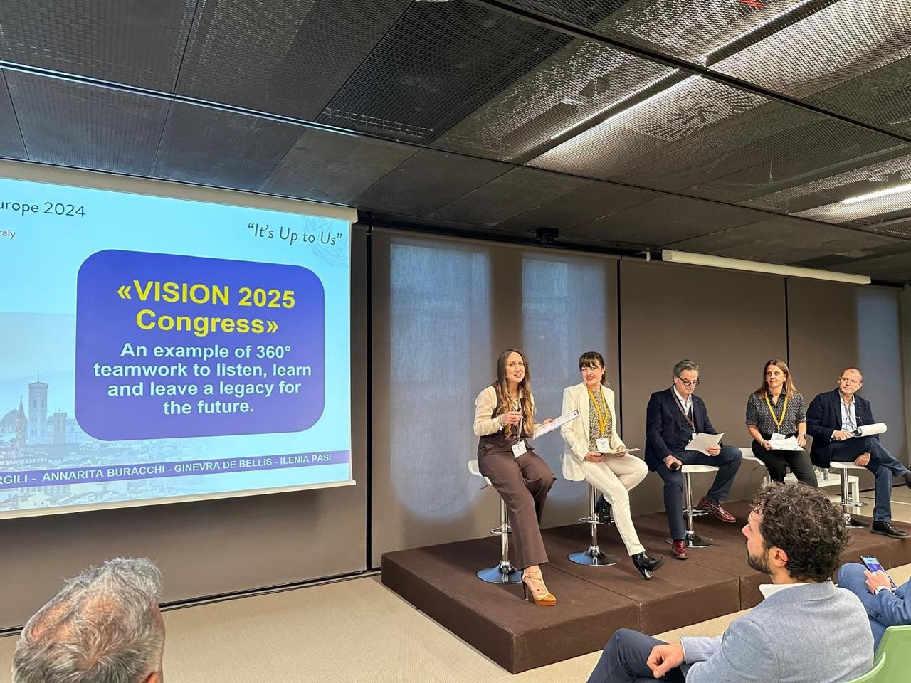 Panel discussion at the "VISION 2025 Congress," featuring five speakers discussing teamwork and legacy for the future, with a presentation slide in the background.