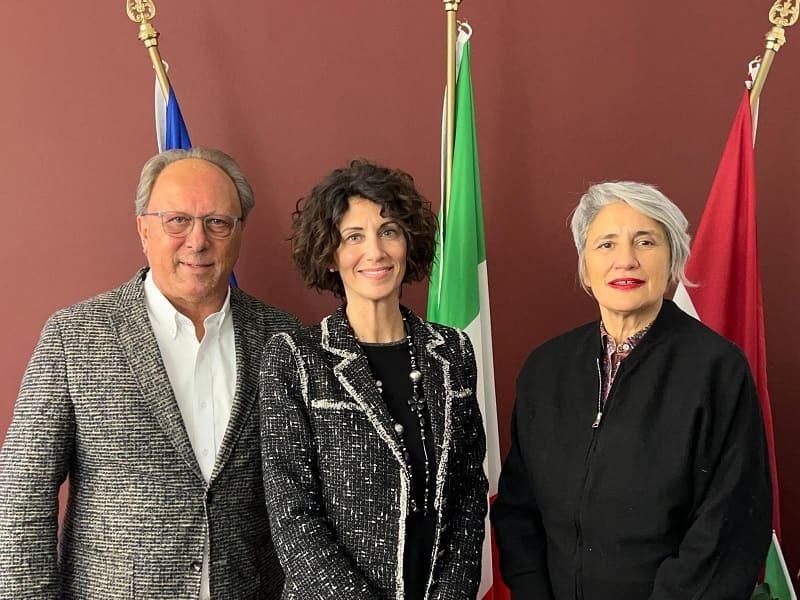 Tre persone in piedi davanti a bandiere italiane e di altri paesi, per la presentazione di Didacta Trentino