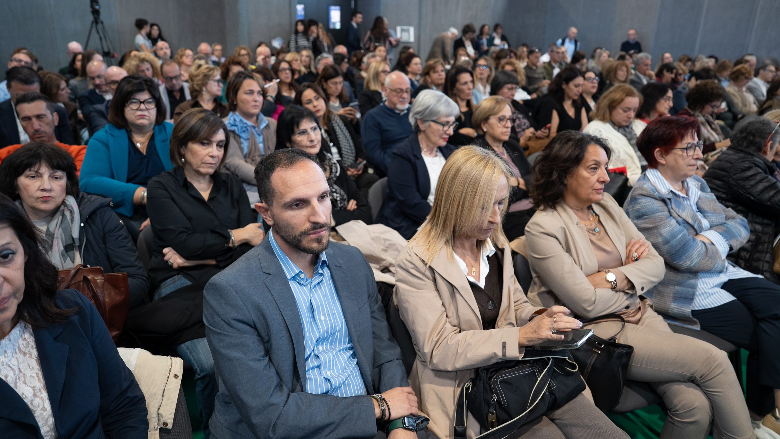 Partecipanti seduti ascoltano una conferenza in una sala gremita.